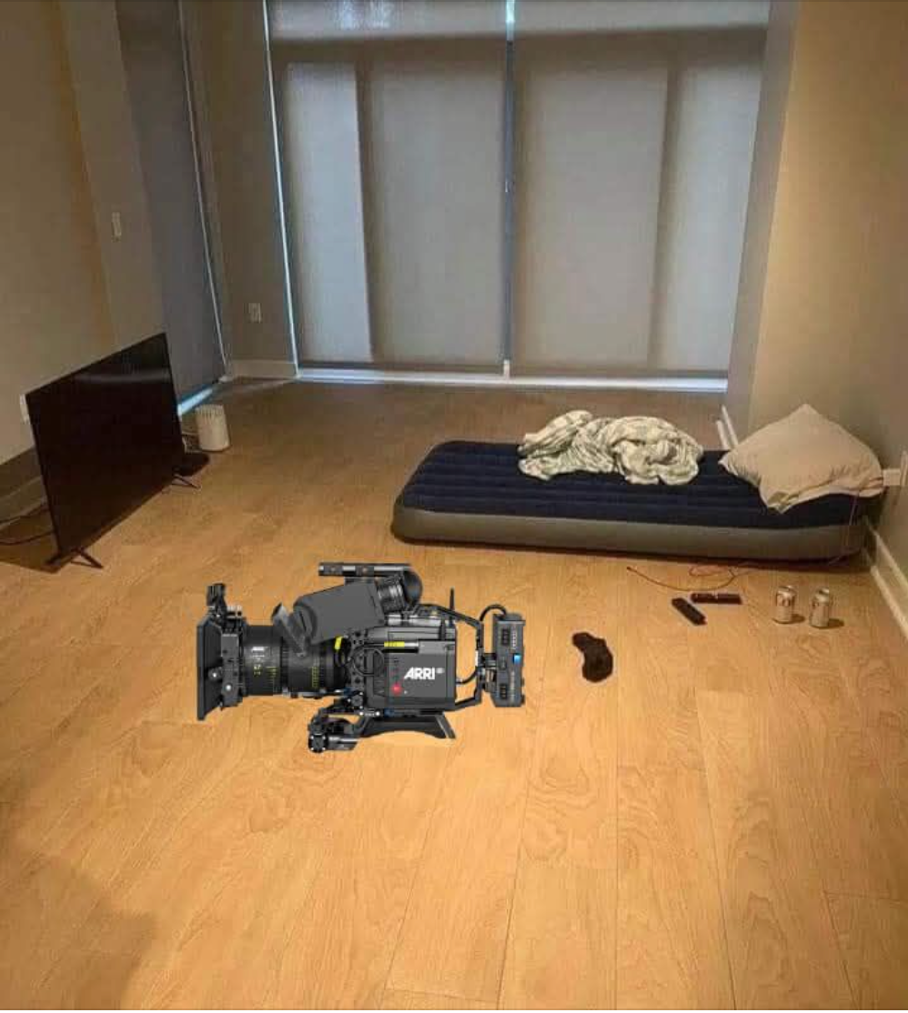 A sparse room with a mattress, a television, a camera and open floor space.